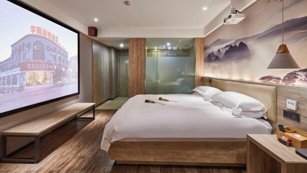 Een moderne hotelkamer met een groot bed, een bank, een projectiescherm en een muurschildering.