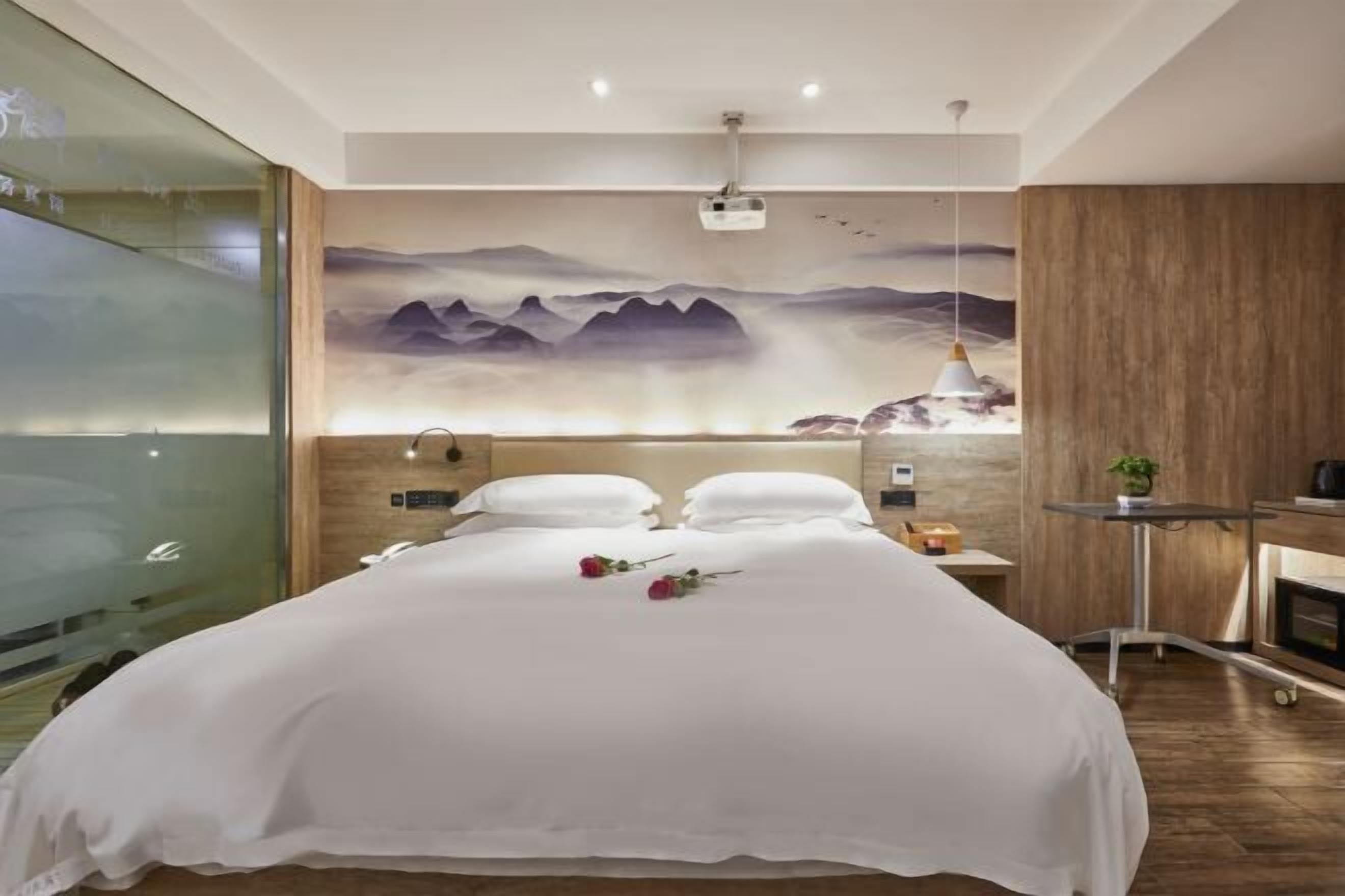 Une chambre d’hôtel moderne avec un grand lit, un tableau au mur, un bureau avec une lampe et une petite table avec une plante.