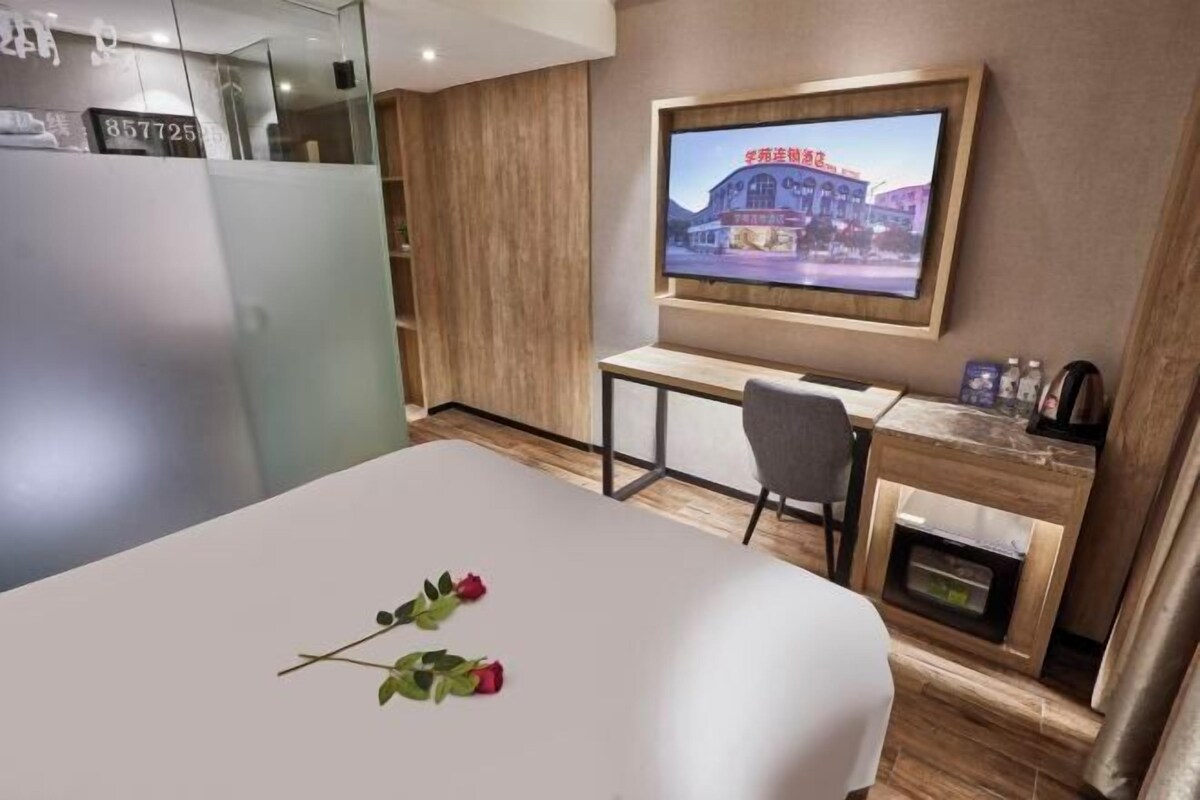 A hotel room with a bed, a desk, a chair, a television mounted on the wall, and a small cabinet below the desk.