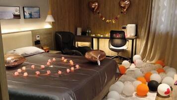 A hotel room with a bed, a desk, and a chair. There are balloons on the floor and a string of lights on the bed.