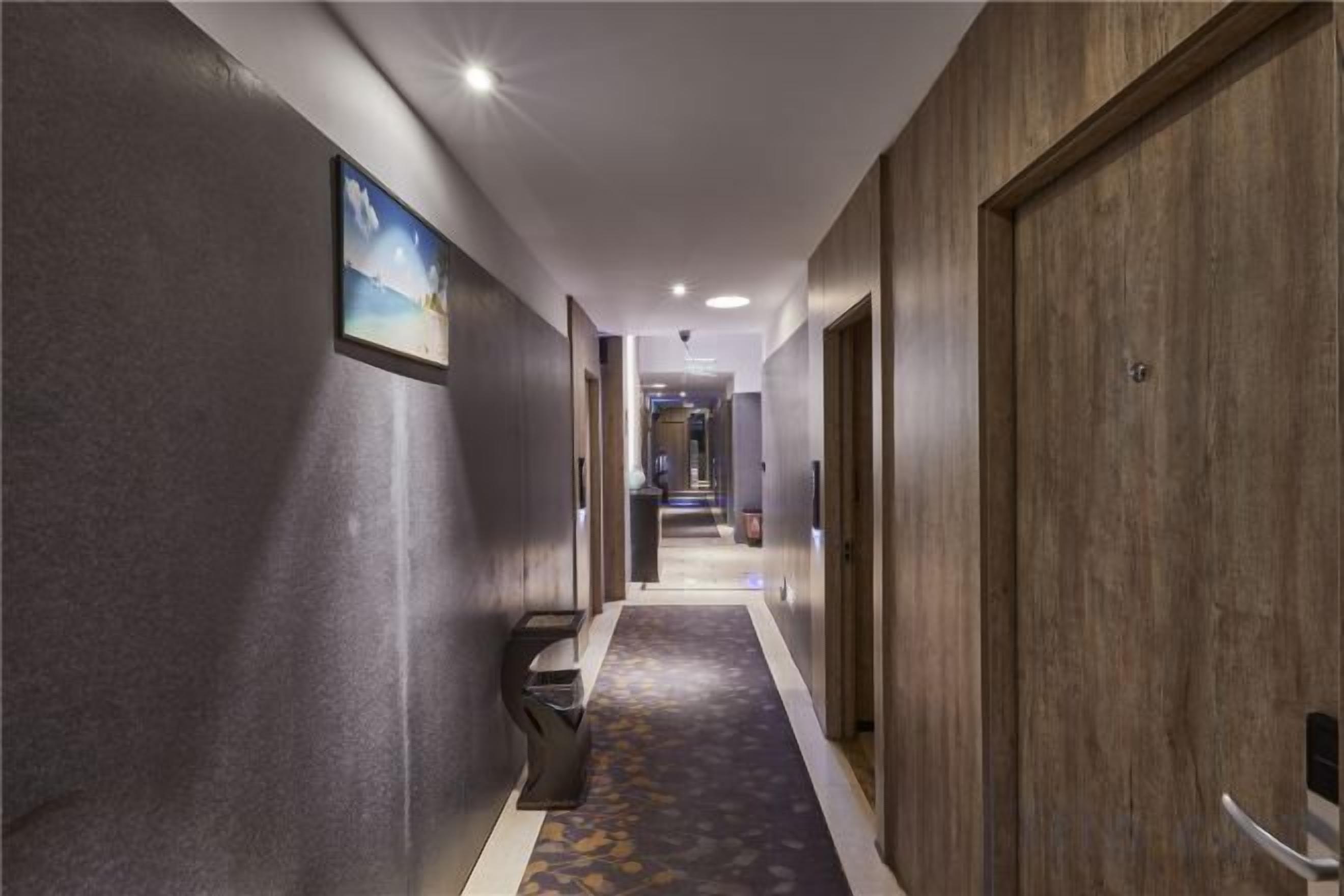 Un pasillo con piso alfombrado, puertas de madera y un cuadro en la pared.