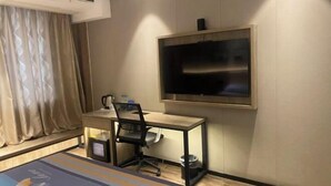 Een hotelkamer met een bureau, stoel, televisie aan de wand en een raam met gordijnen.
