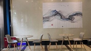 Een modern interieur met een groot abstract schilderij, een ronde tafel en vier stoelen met houten poten.