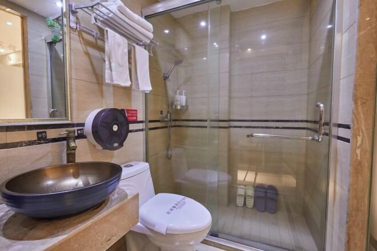 A bathroom with a glass-enclosed shower, a sink with a bowl basin, a toilet, and a mirror.