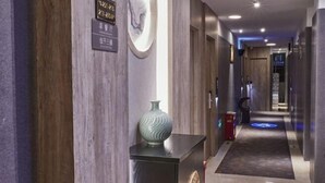 Een hotelgang met houten lambrisering, een decoratieve vaas en een blauw verlicht pad.
