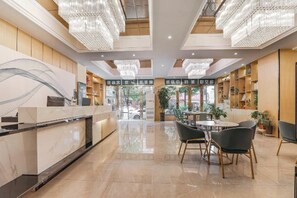 Een hotel lobby met een receptiebalie, een zithoek en uitzicht op de straat.