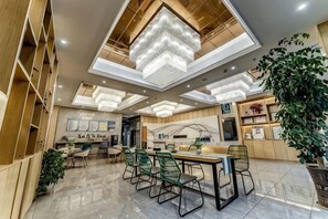 A modern hotel lobby with a central dining area, wooden shelving, and a large chandelier. - Kester Business Hotel (Qianxi)