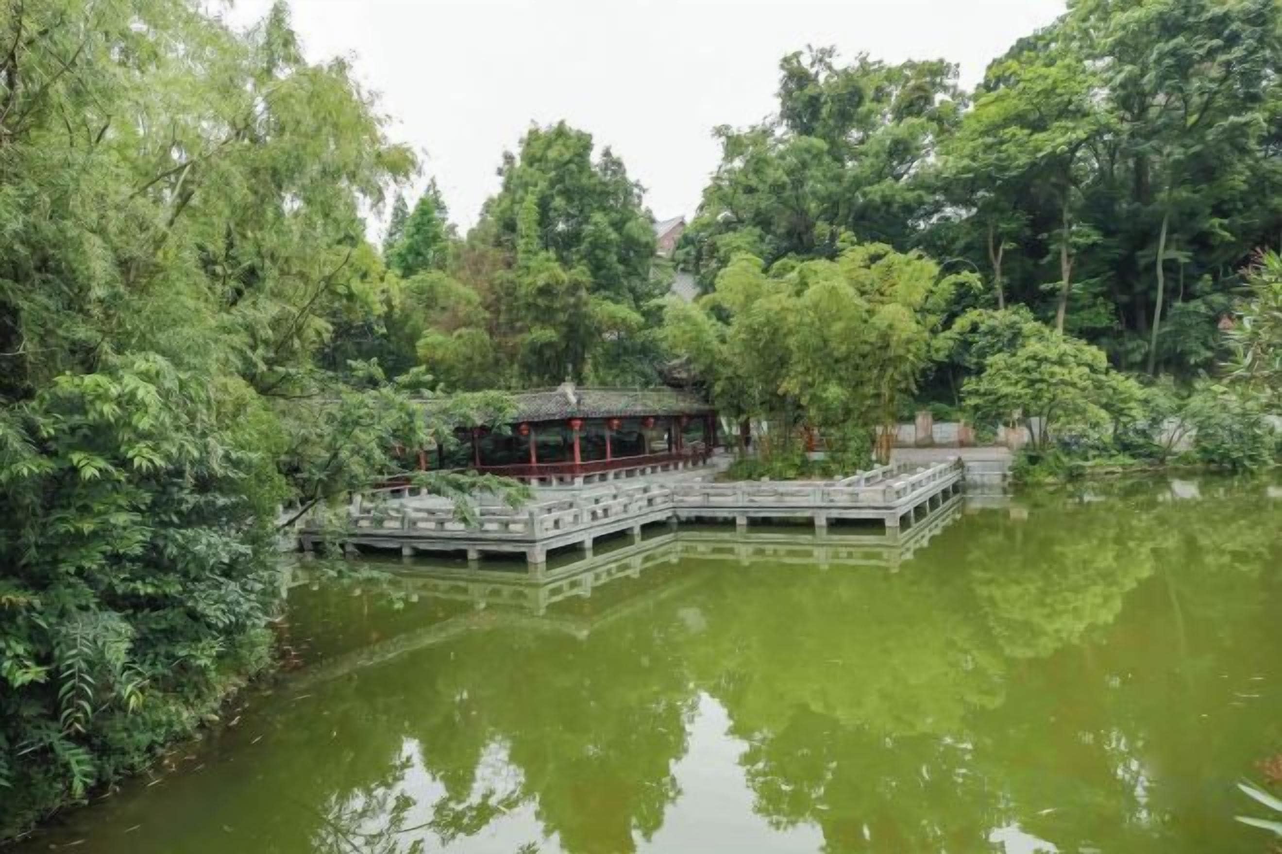 A traditional pavilion on a lake surrounded by dense greenery.