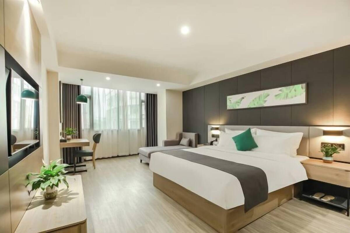 A modern hotel room with a large bed, a desk, a chair, and a potted plant.