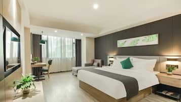 A modern hotel room with a large bed, a desk, a chair, and a potted plant.