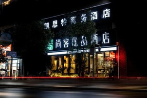 A hotel with illuminated signage in a foreign language, a visible entrance, and a parking area in the foreground.