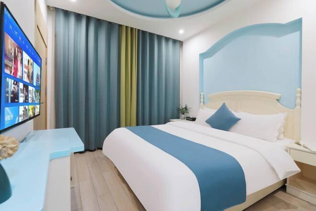 A hotel room with a bed, a TV mounted on the wall, a desk, and a curtain.