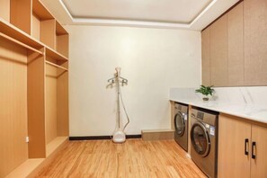 Un cuarto de lavandería con lavadora, secadora y una lámpara de pie.