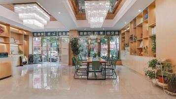 A hotel lobby with a central dining area, large windows, and potted plants.