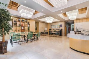 Un vestíbulo de hotel con mostrador de recepción, zona de comedor con sillas verdes y una lámpara de araña grande.