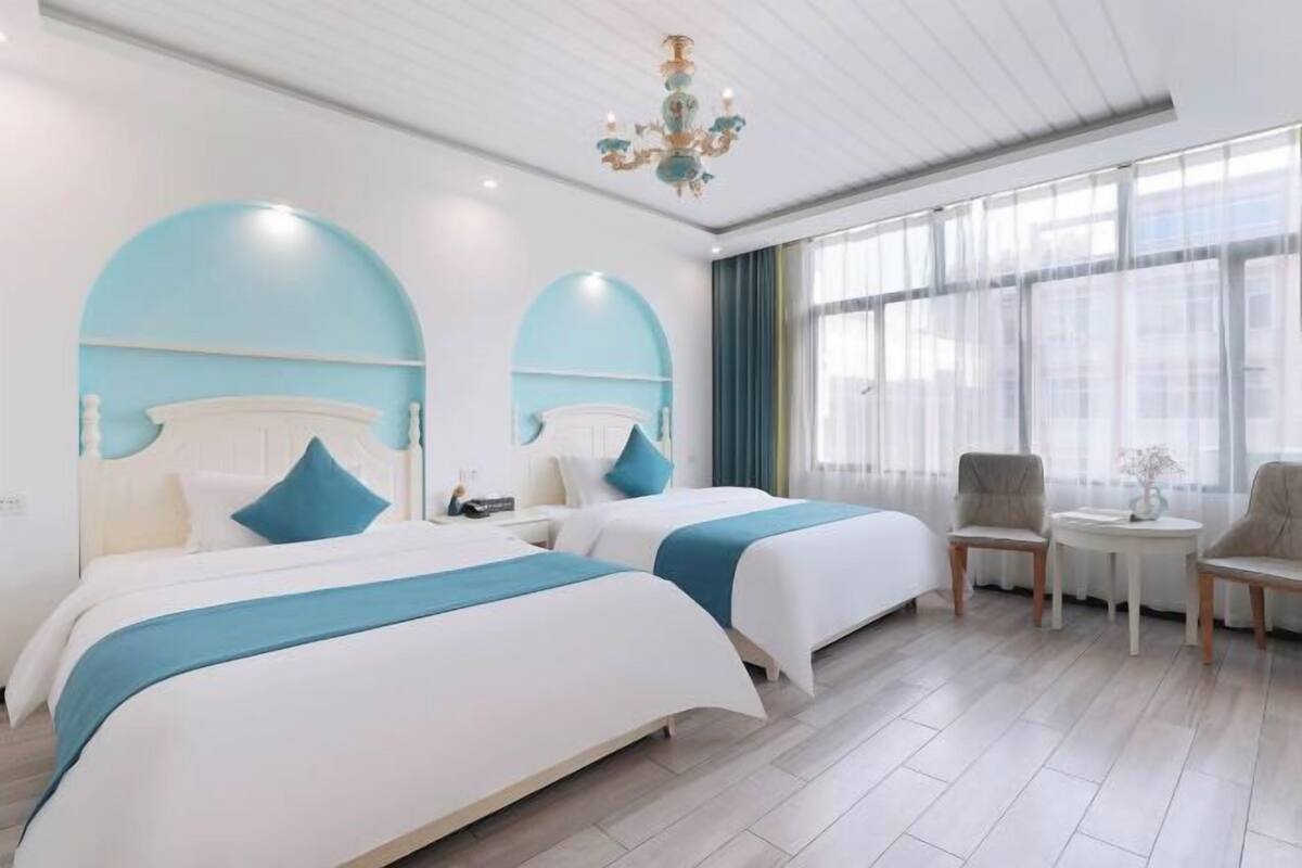 A hotel room with two beds, a chandelier, a small table, and a chair.