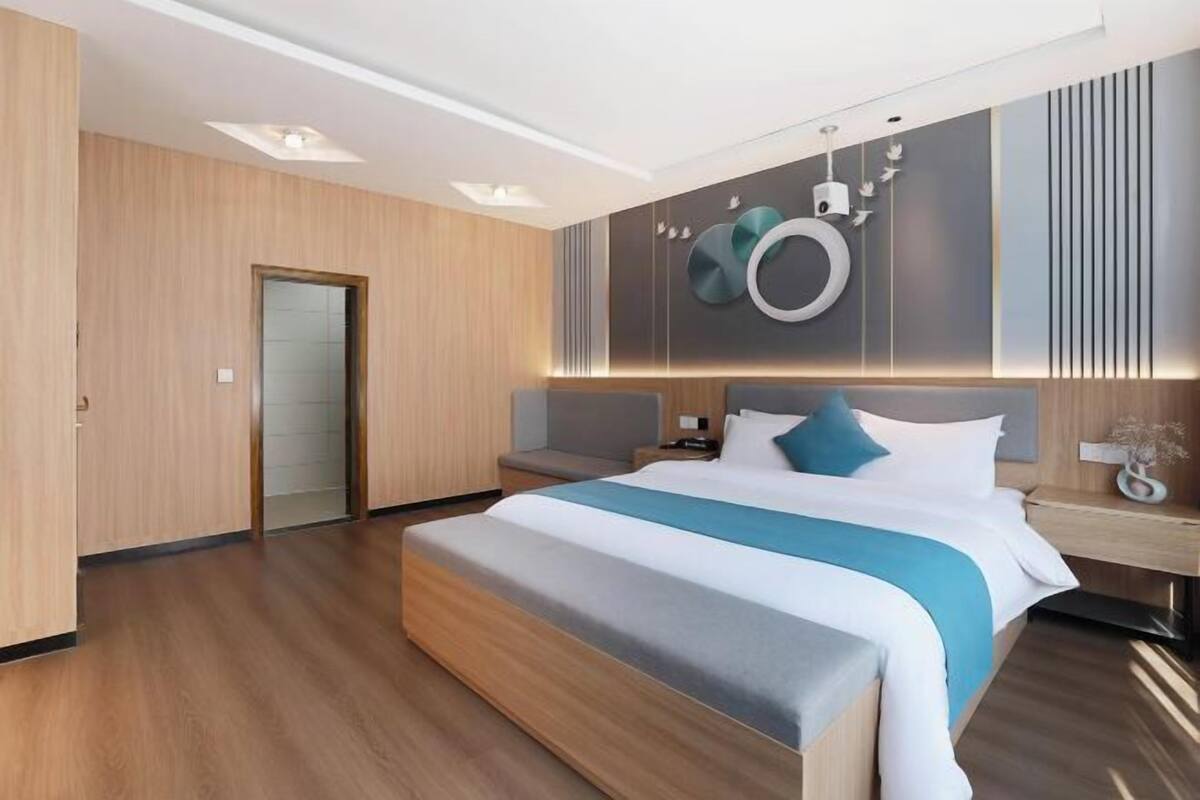 A modern hotel room with a large bed, a bedside table, a nightstand, and a wall-mounted light fixture.