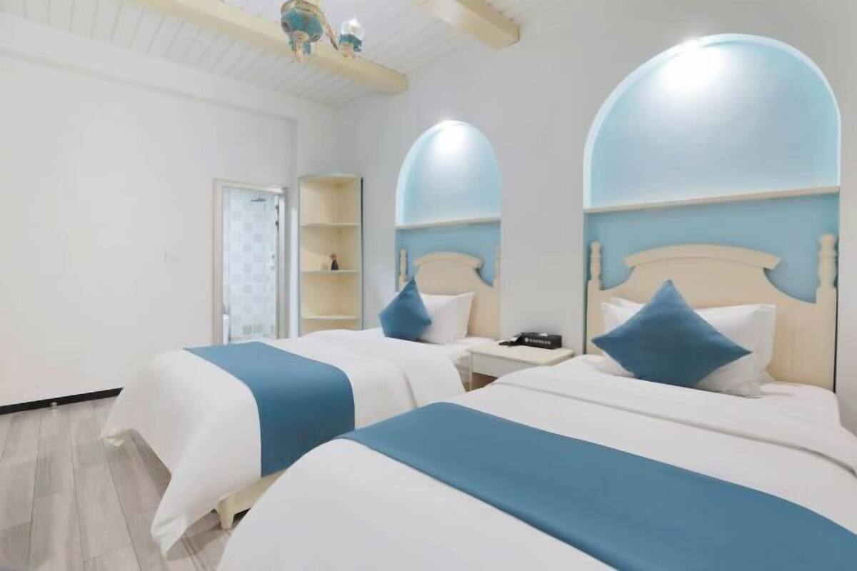 A hotel room with two beds, a nightstand, a mirror, and a shelf with a decorative item.