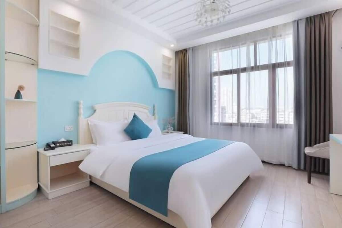 A hotel room with a bed, bedside table, and a window with curtains.