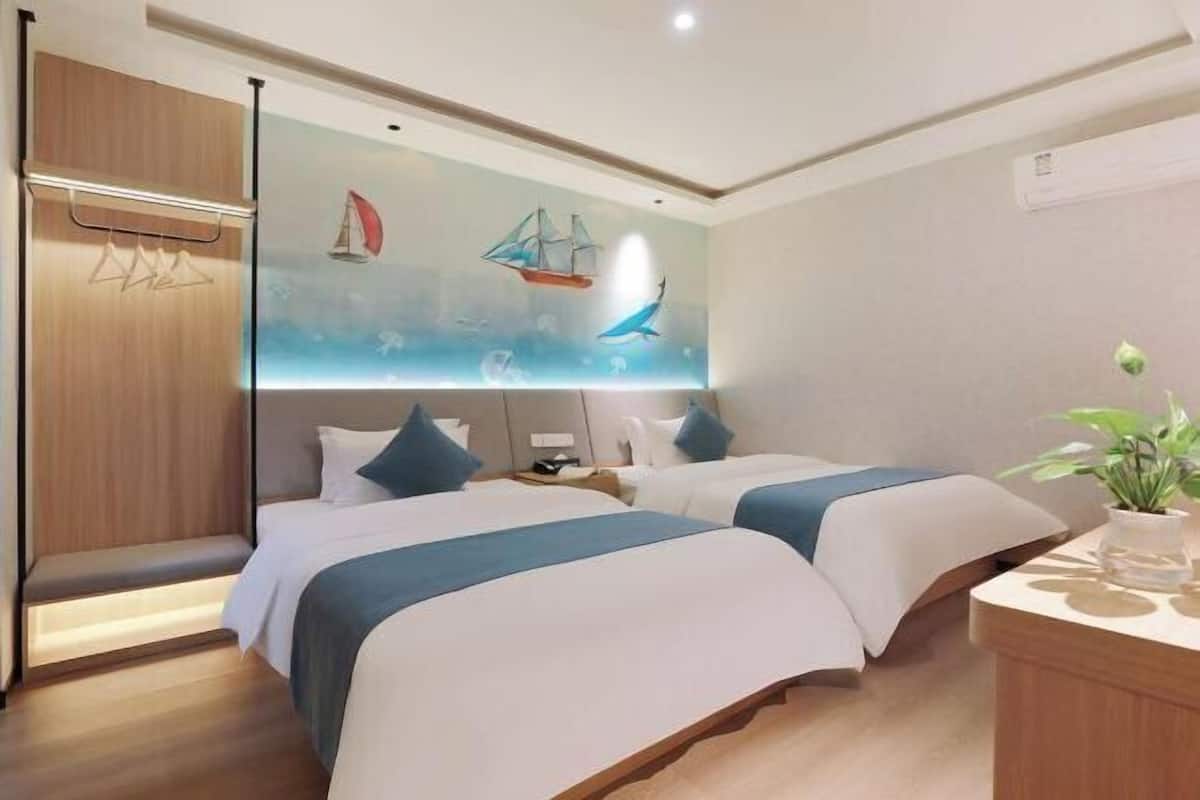 A hotel room with two beds, a wooden wardrobe, a desk, and a wall mural with nautical themes.