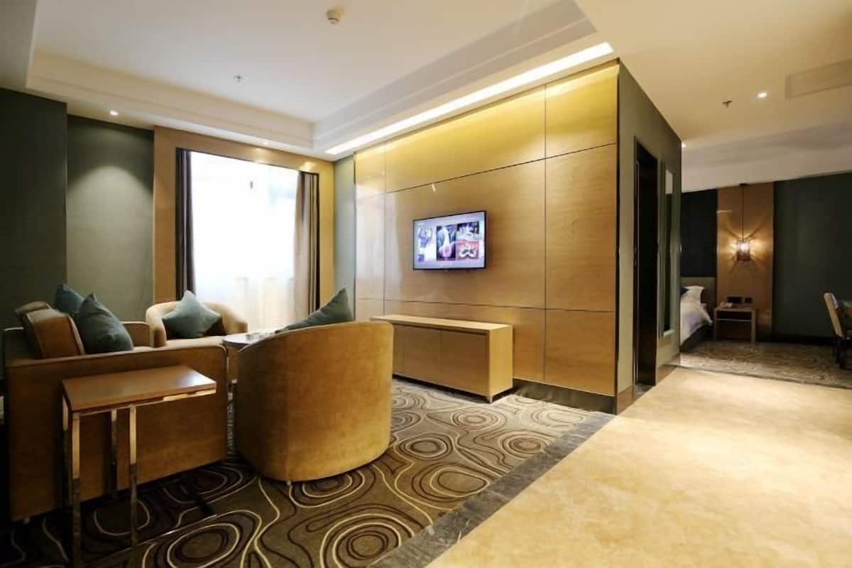 A modern hotel room with a sofa, armchair, and a flat-screen TV mounted on the wall.