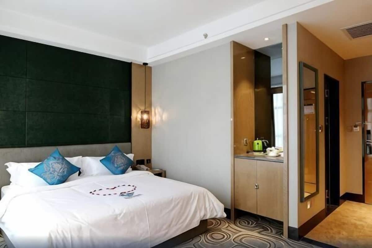 A hotel room with a bed, a nightstand, a mirror, a wardrobe, and a small kitchenette area.