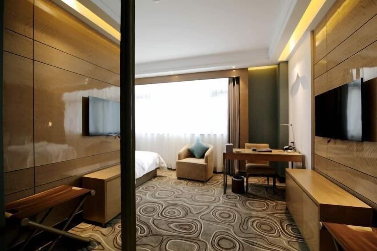 A hotel room with a bed, a desk, a chair, a television, and a patterned carpet.