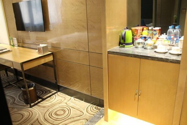 A modern hotel room with a wooden cabinet, a small table with a tissue box, a trash can, and a television mounted on the wall. - Xiya Inn (Lanzhou)