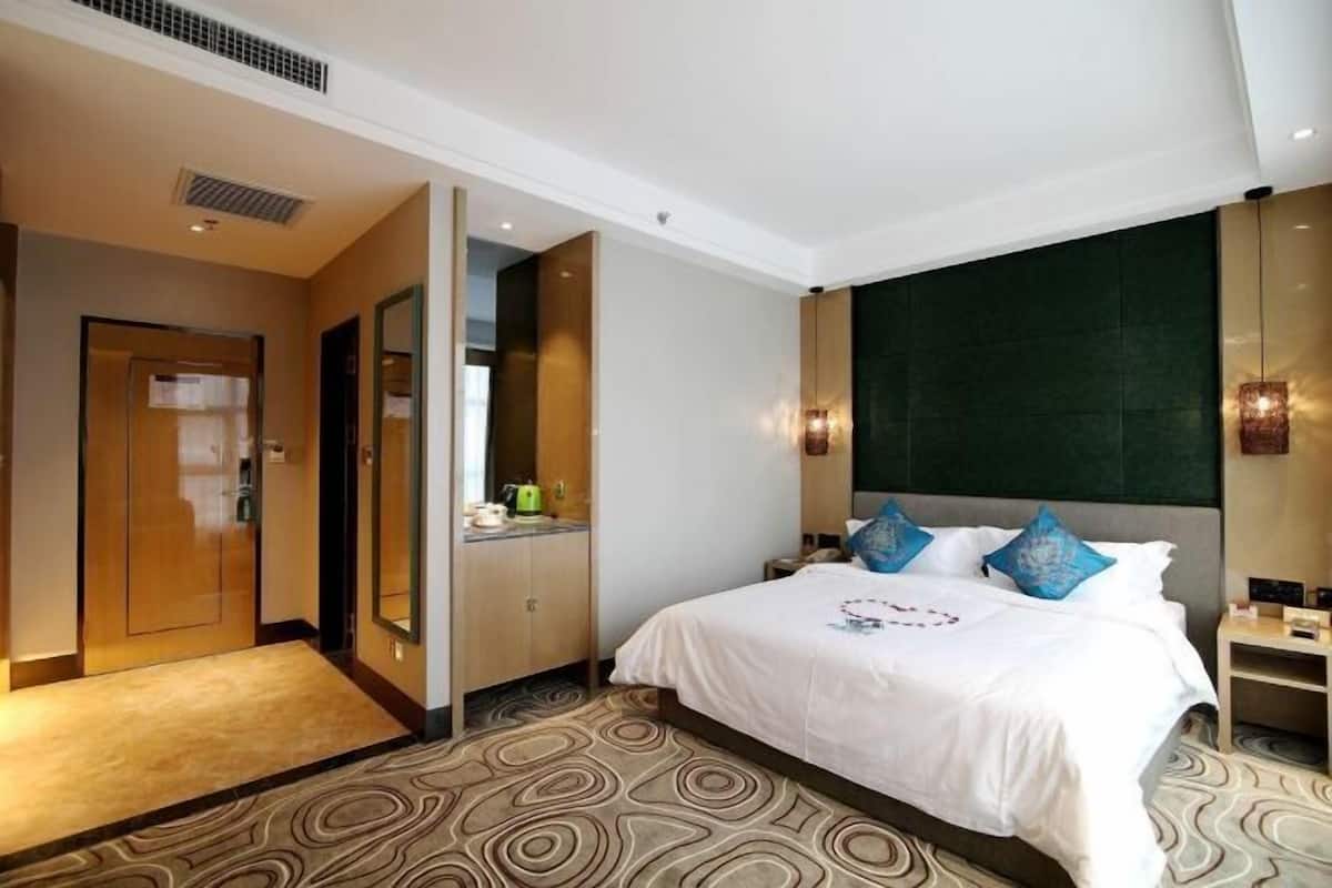 A hotel room with a bed, a mirror, a wardrobe, and a small table with a lamp.