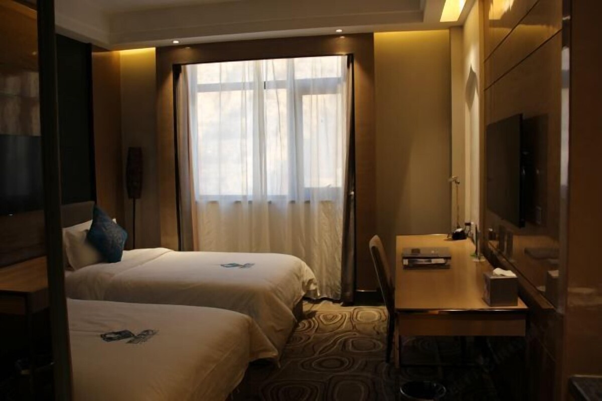 A hotel room with two beds, a desk, a chair, a television, and a large window with curtains.
