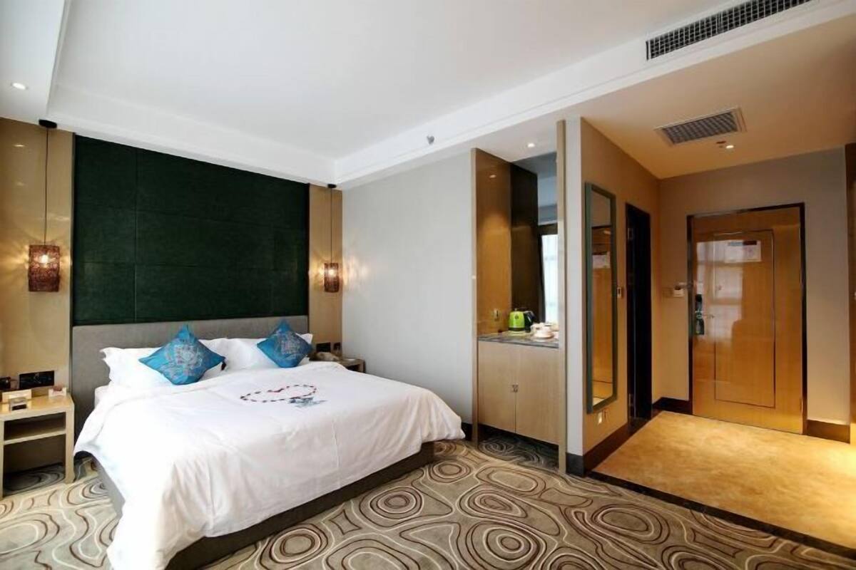 A hotel room with a large bed, a bedside table, a wardrobe, and a bathroom visible through an open door.