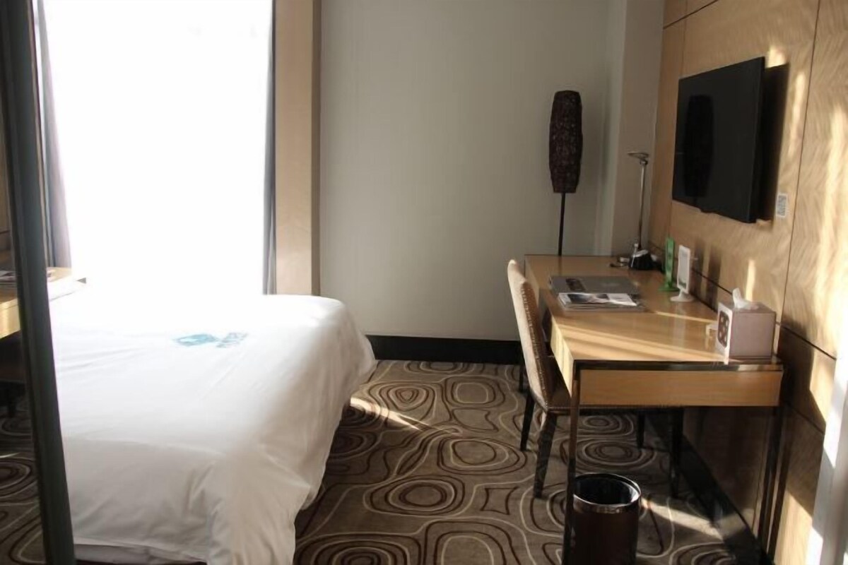 A hotel room with a bed, a desk, a chair, a television, and a patterned carpet.