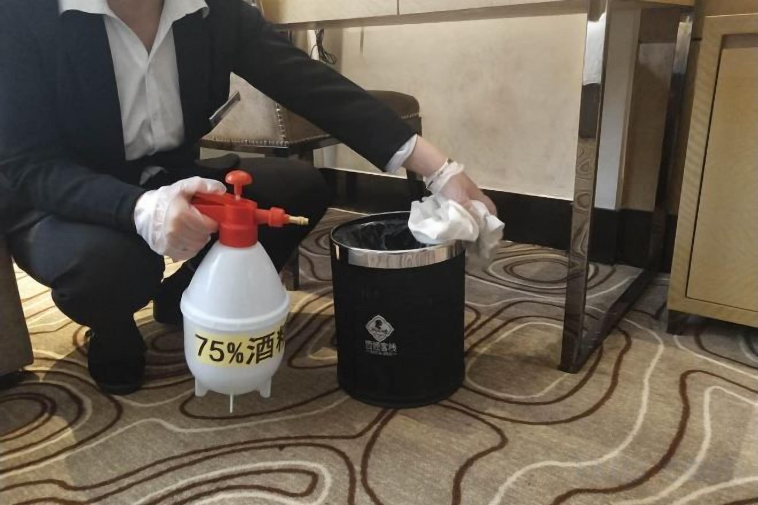 A person in a suit using a spray bottle and a cloth on a carpeted floor.