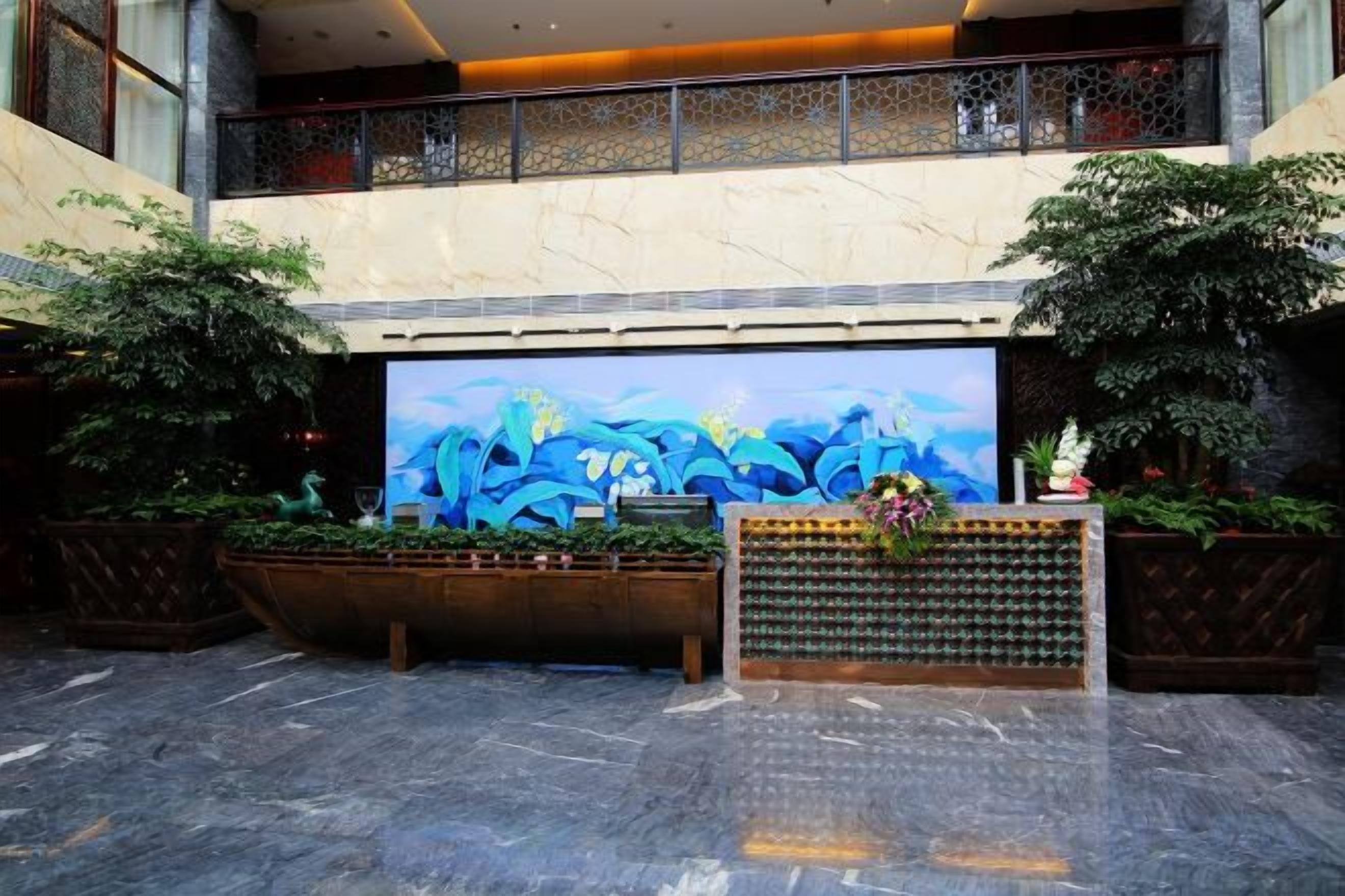 Un vestíbulo con una pantalla digital grande, plantas en macetas y un mostrador de recepción.