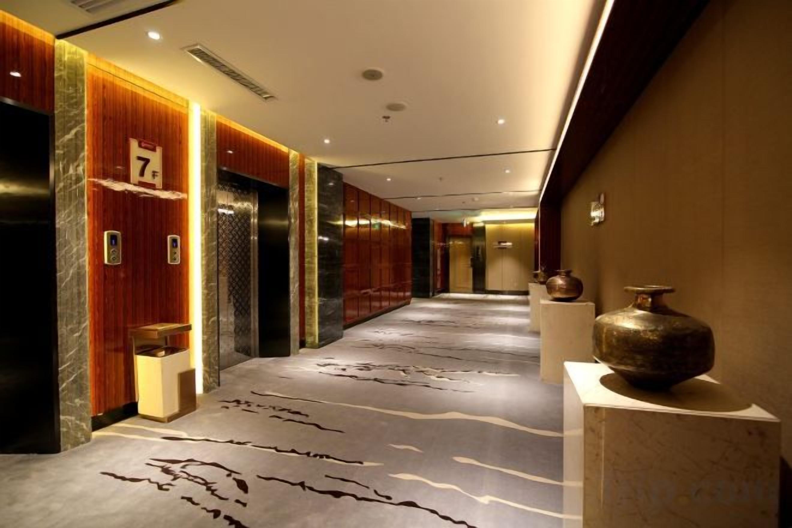 Un pasillo de hotel con ascensores, una recepción y un jarrón decorativo.