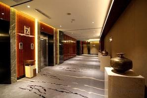 A hotel corridor with elevators, a reception desk, and a decorative vase. - Xiya Inn (Lanzhou)