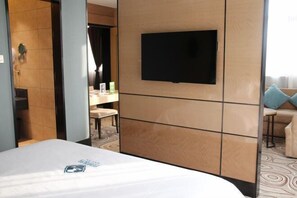 A hotel room with a bed, a television mounted on the wall, a bathroom with a shower, and a seating area with a table and chairs. - Xiya Inn (Lanzhou)