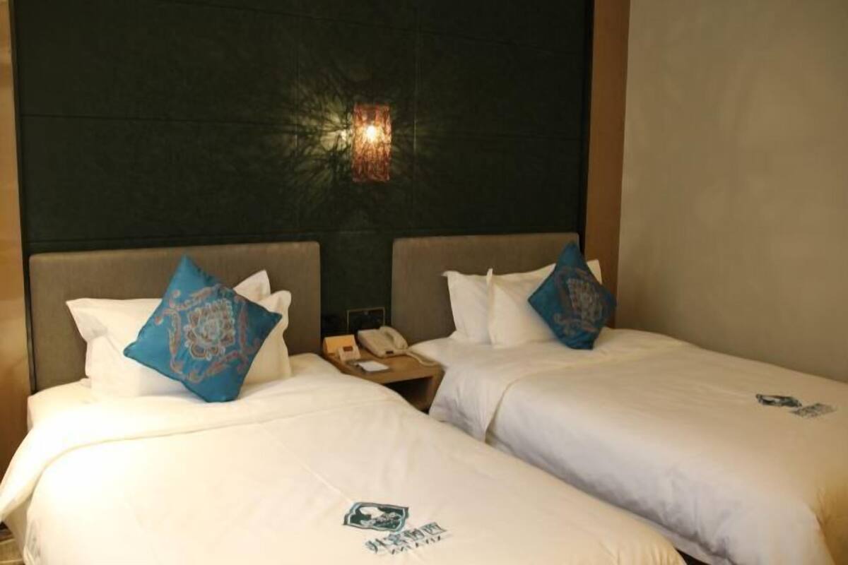 A hotel room with two beds, each with a pillow and a headboard. There is a nightstand between the beds with a phone and a lamp.