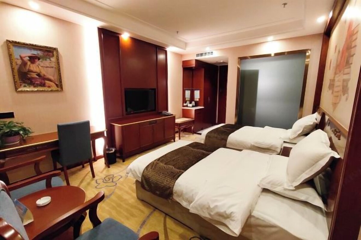 Ein Hotelzimmer mit zwei Betten, einem Schreibtisch, einem Sessel, einem Fernseher und einem Bild an der Wand.