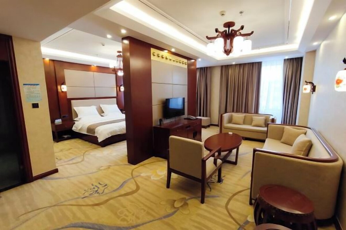 Ein Hotelzimmer mit einem Bett, einem Fernseher, einem Sofa, einem Couchtisch und einem kleinen Hocker.