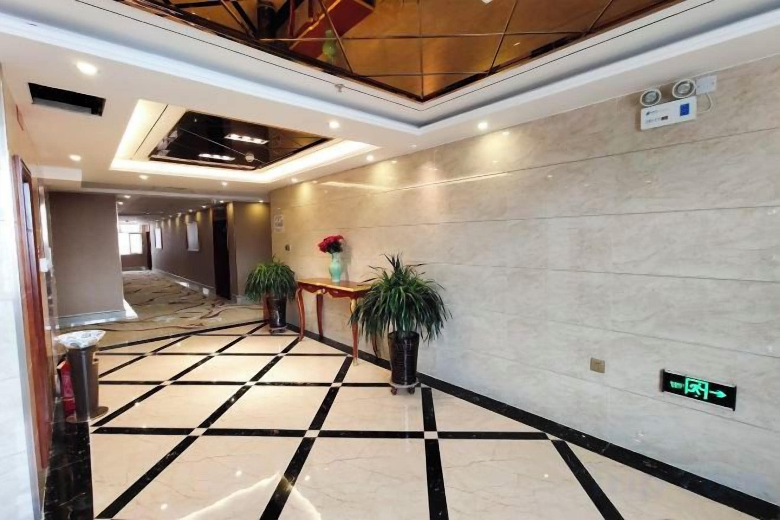Pasillo de hotel con mostrador de recepción, plantas en macetas y un letrero digital que indica el camino al vestíbulo.