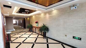 Pasillo de hotel con mostrador de recepción, plantas en macetas y un letrero digital que indica el camino al vestíbulo.