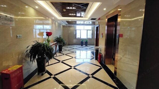 A hotel lobby with a check-in counter, a reception desk, a large potted plant, and a tiled floor. - Yixin Hotel (Emin)