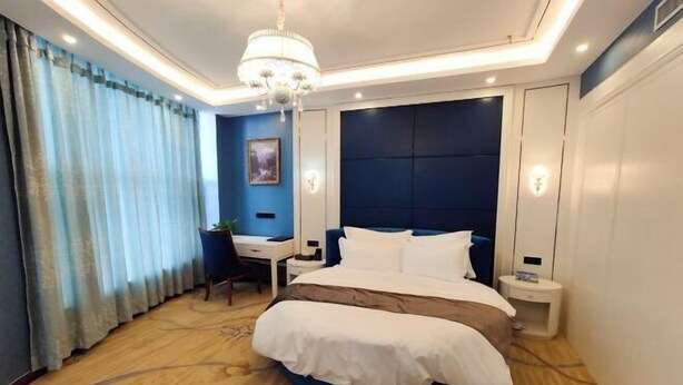 Ein Hotelzimmer mit einem großen Bett, einem Schreibtisch, einem Sessel, einer Chandelüster und Blick ins Freie.
