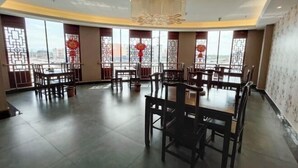 Ein Restaurant mit mehreren Tischen und Stühlen, großen Fenstern mit Verzierungen und einem modernen Deckenstil.