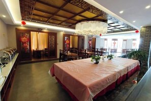 A restaurant with a long table, chairs, and a ceiling with a decorative pattern. - Yixin Hotel (Emin)
