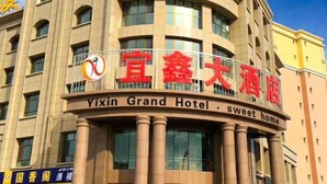 Ein Hotelgebäude mit einem Schild, auf dem "Yixin Grand Hotel" und "süßes Zuhause" steht.