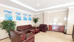 Eine Lobby mit einem braunen Ledersofa, einem Holztisch und einem Schrank. An den Wänden befinden sich Poster und es steht ein Blumentopf dort.