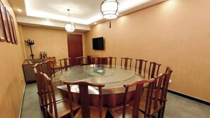 A conference room with a round glass table surrounded by wooden chairs, a television on the wall, and a door in the background. - Yixin Hotel (Emin)