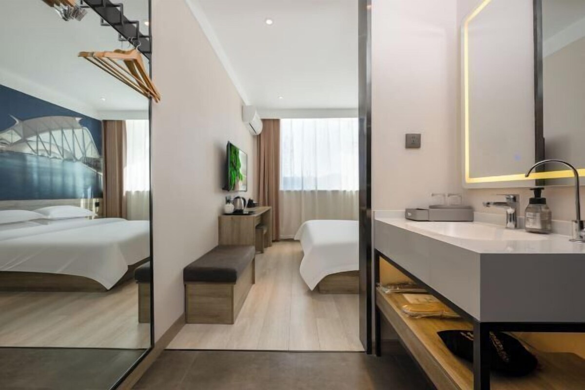 Ein modernes Hotelzimmer mit zwei Betten, einem großen Spiegel, einem Waschtisch und Blick auf ein Gebäude durch das Fenster.